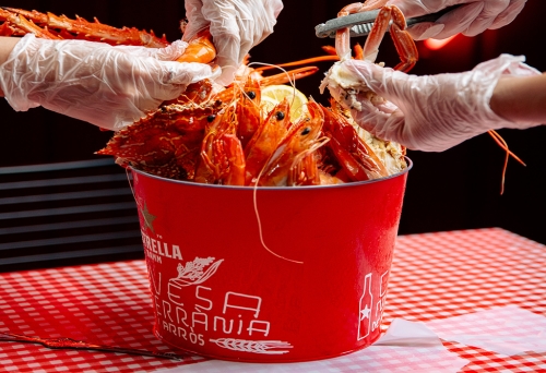 Bucket of crab with two pairs of gloved hands grabbing pieces