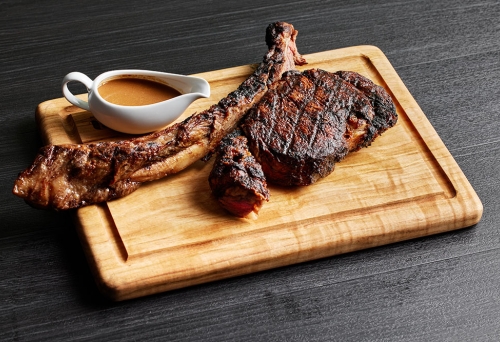 T-bone steak on chopping board with sauce cup
