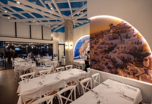Tables and chairs with white tablecloths and mural on wall inside Santorini Restaurant, Newstead