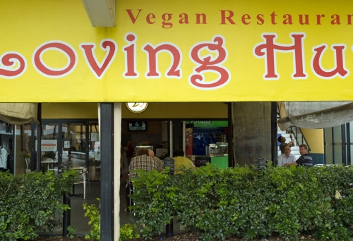 Loving Hut sign and hedge with diners sitting outside Loving Hut cafe Mt Gravatt