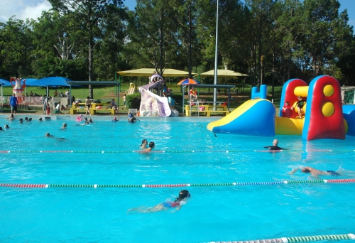 People swimming in Newmarket Pool with giant floating castle with children playing on it.