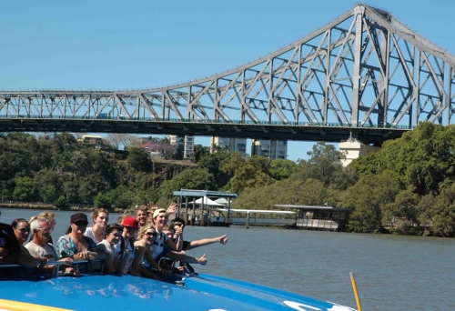 Passengers waving on board Rivercat Ferry in fron of  Brisbane's Story Bridge.