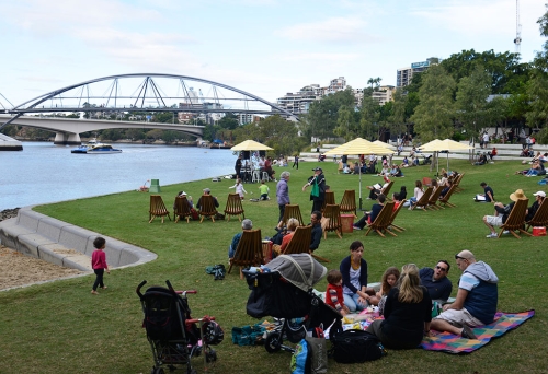 People lying on grass by the Brisbane River at the Sunday Sessions on the Green