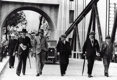Old black and white photo of five men wearing suits and hats walking along Indooroopilly