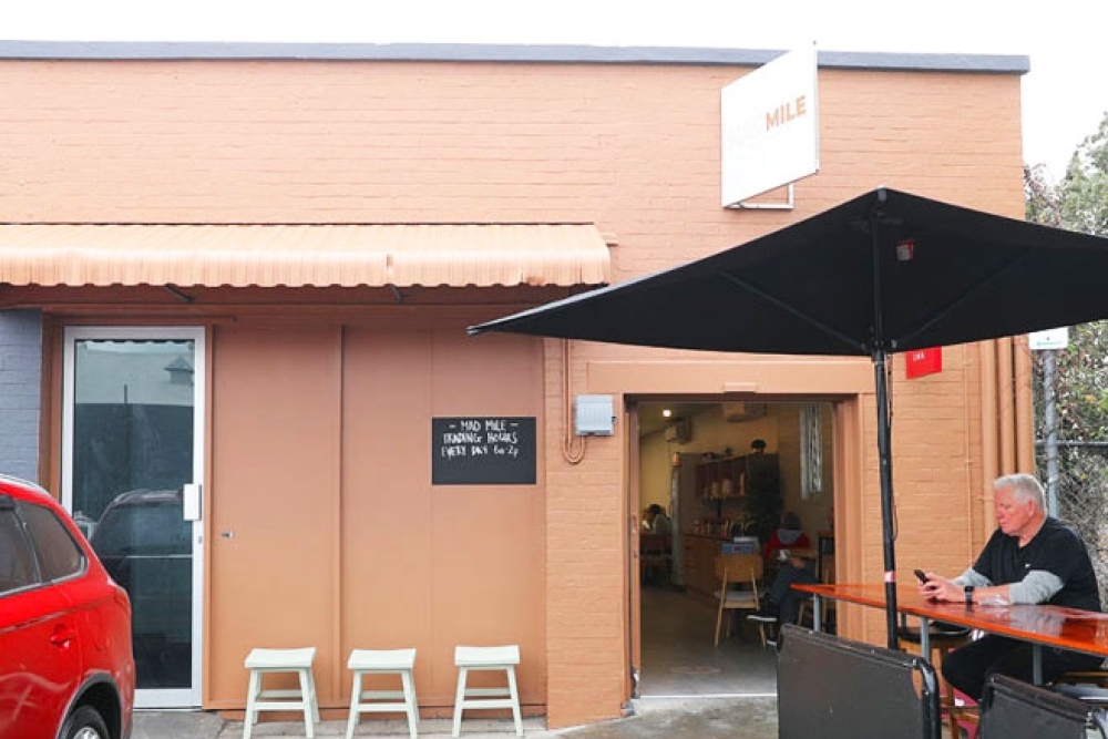 Man sitting under an umbrella at a table outside Mad Mile Coffee