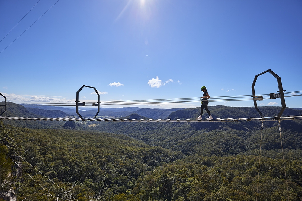 Woman on an 80-metre wobbly bridge at The Arête Via Ferrata Tour at Happitat Adventure Park 