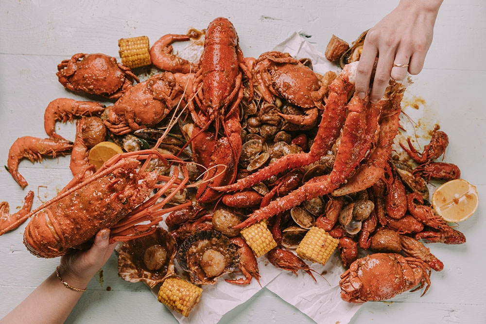 Two hands grabbing pieces of crab at Krabby’s Crab Boil, The Barracks, Petrie Terrace