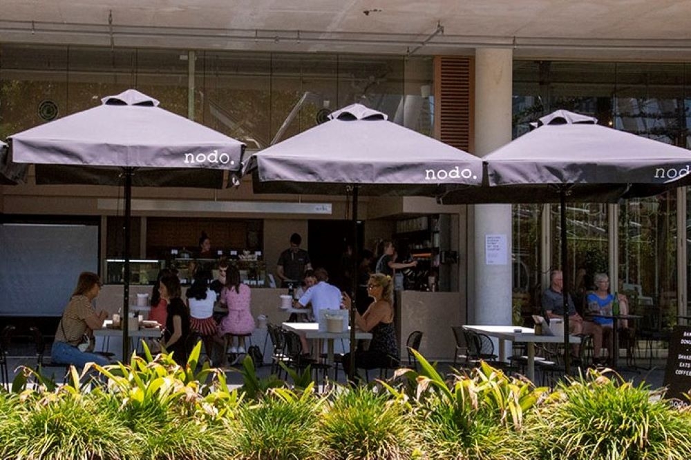 People sitting under umbrellas in courtyard at Nodo South 