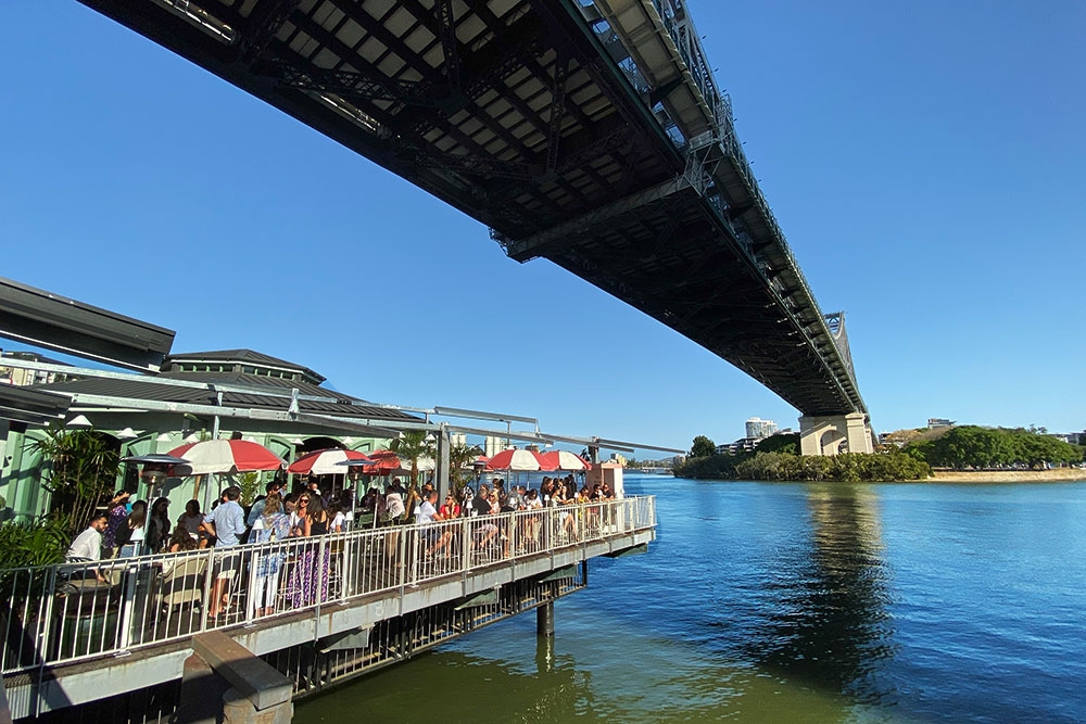 People dining at open air cafe under bridge next to Brisbane River