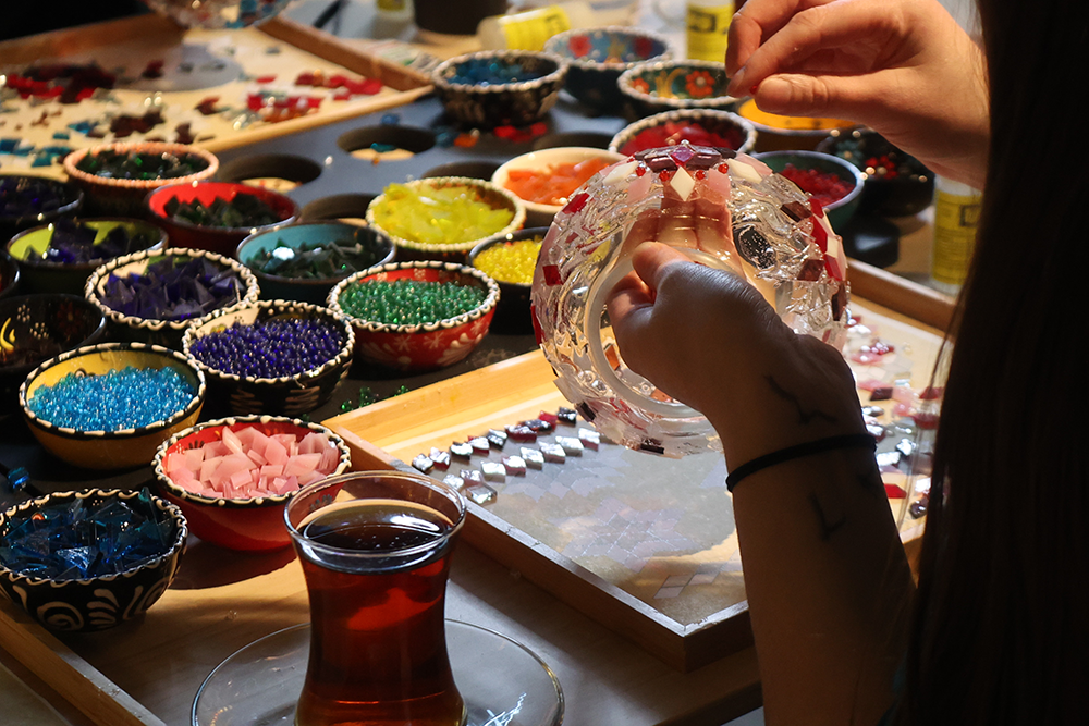 A lady glueing mosaic tiles on a glass vase