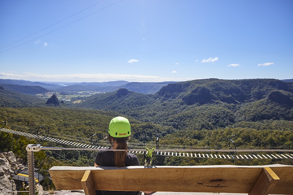 Woman sitting on 12-metre cantilevered platform on The Arête Via Ferrata Tour at Happitat Adventure Park