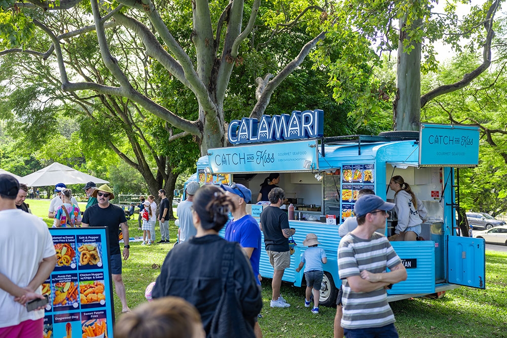 People standing around food trucks at the Easter Weekend at Roma Street Parkland