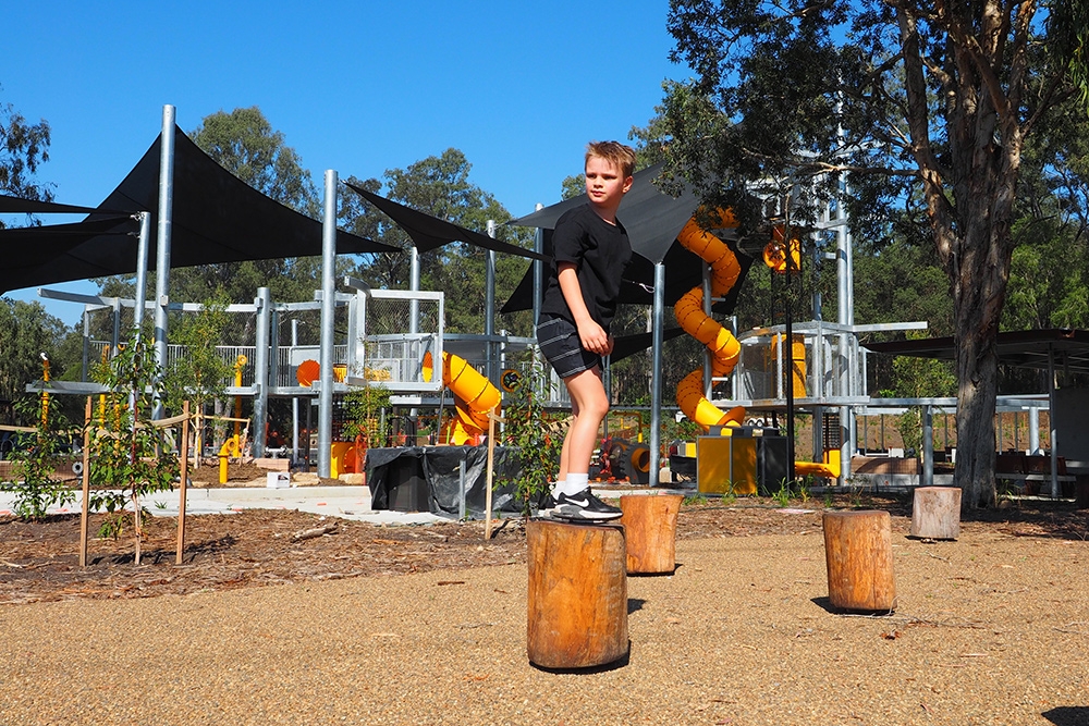 Boy standing on logs in playground, Archerfield Wetlands District Park