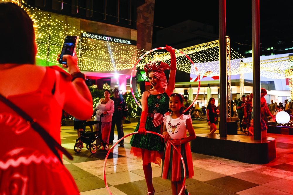 Woman taking of photo of child with hula hoop roving entertainer at Christmas at Nicholas St Precinct