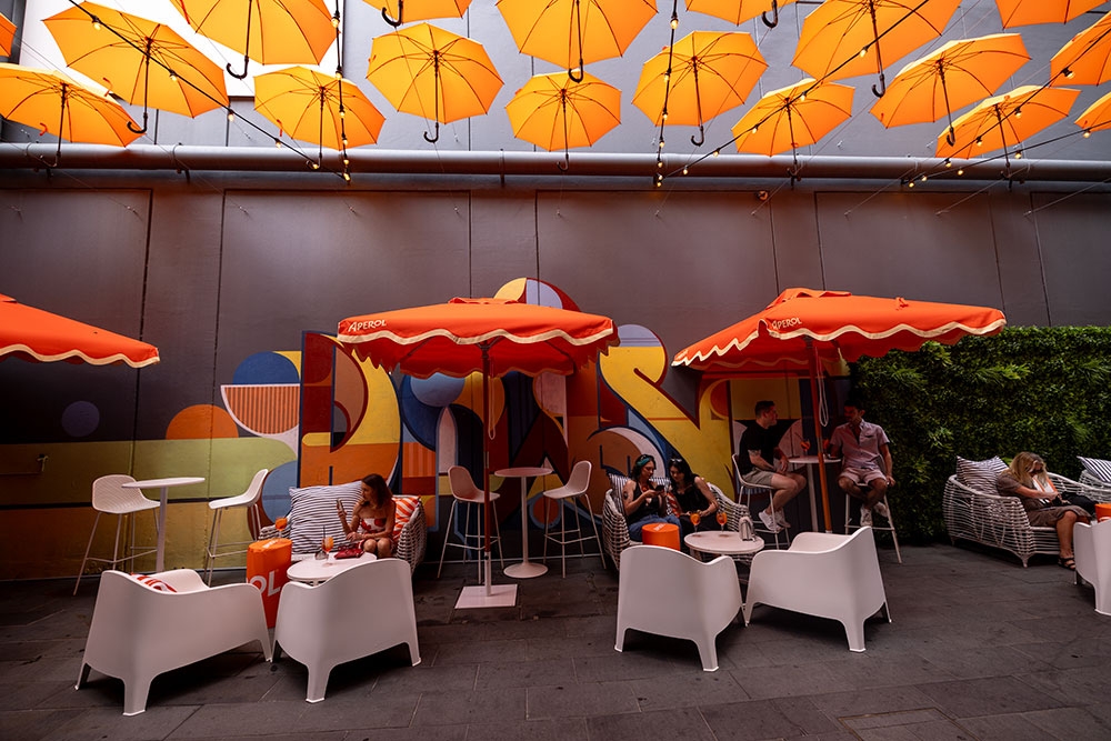People seated on patio chairs under orange umbrellas Doughcraft Lane 