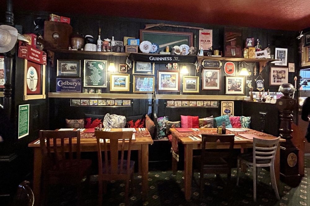 Two wooden chairs and tables inside Fox & Hounds Country Inn, Wongawallan with British memorabilia on the back wall