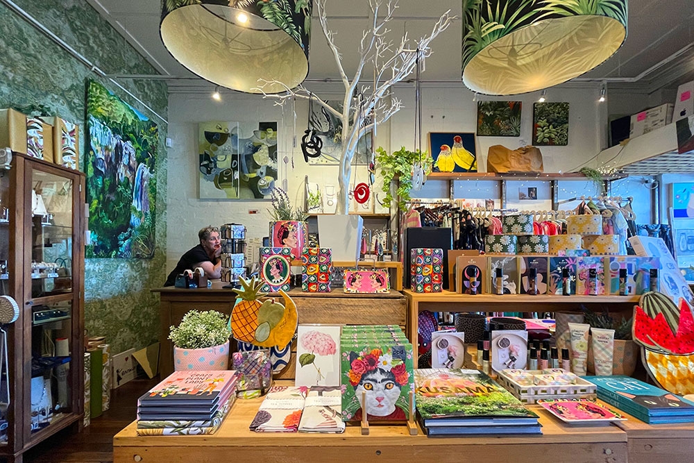Staff member behind counter with homewares for sale inside Green Tangerine, Paddington