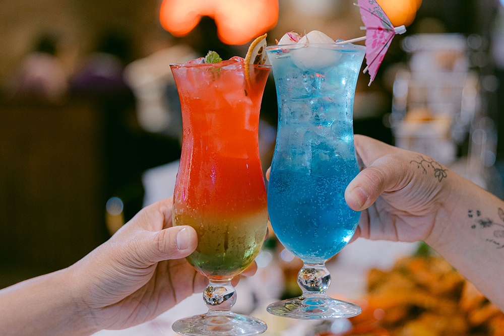 Hands holding a blue and a red cocktail at Krabby’s Crab Boil, The Barracks, Petrie Terrace
