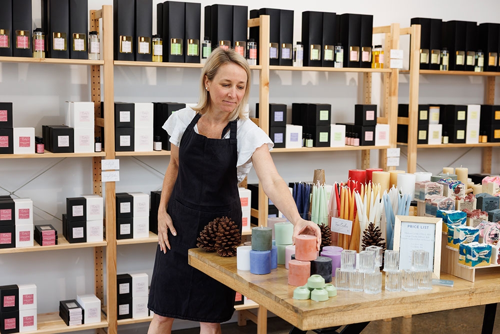 Woman placing candles on the counter inside Lights of Eden home fragrance and gift shop, Albion