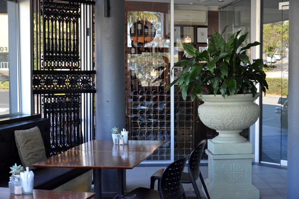 Table and chairs next to large white pot plant inside Little Glass Room Espresso Bar, Mt Gravatt