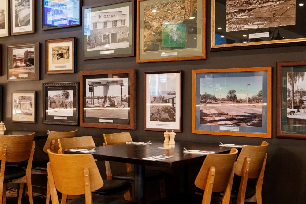 Table and chair against a wall of framed pictures at Morayfield Tavern 