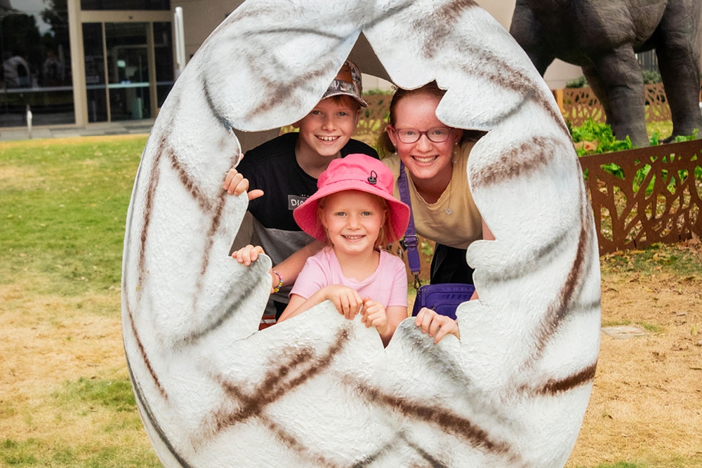 Three smiling children in cracked dinosaur egg for photo opp