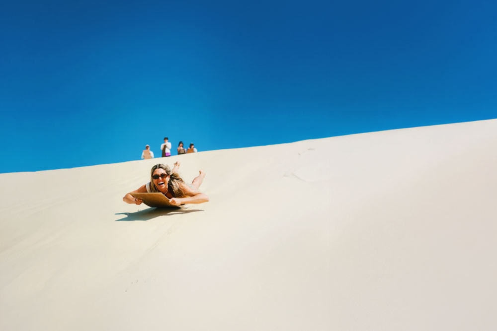 A woman sandboarding down a sand dune