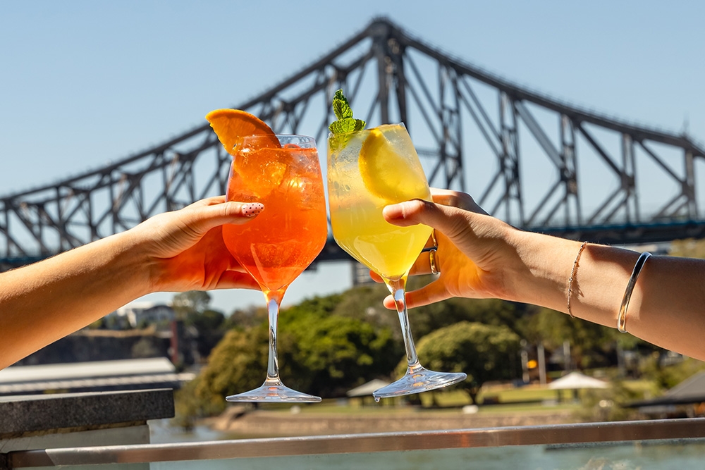 Two drinks clinking in front of the story bridge