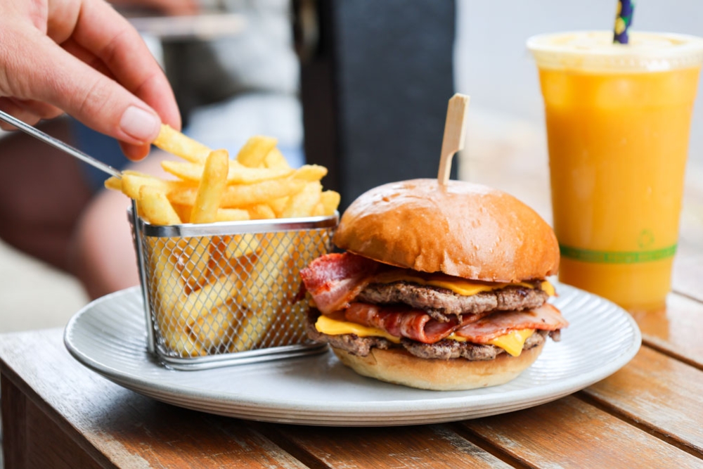 A hand reaching for a chip next to a burger and juice
