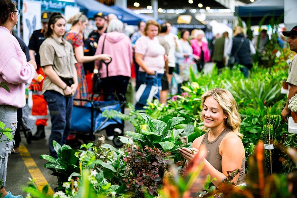 Woman amongst plants with shoppers browsing at the Plantapalooza Plant Festival