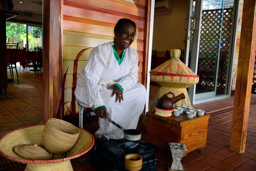Female staff member in traditional dress roasting Ethiopian coffee beans over a little stove outside Mu'ooz African Eritrean Restaurant 